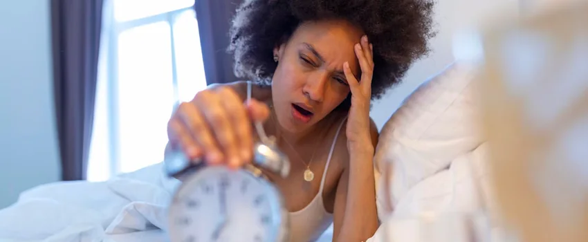 Tired woman waking up in bed and reaching for an alarm clock